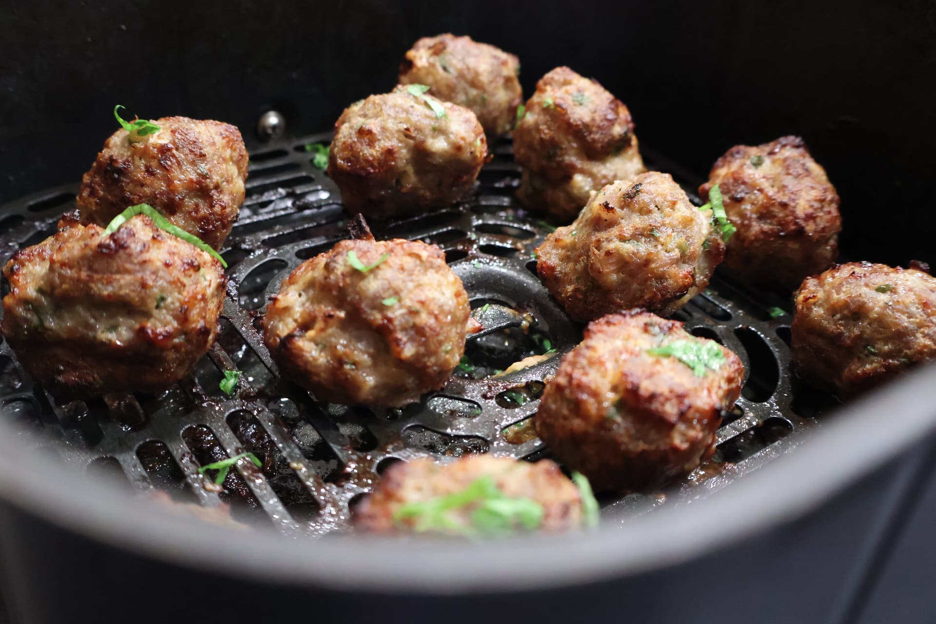 Golden brown meatballs cooking in an air fryer basket, garnished with fresh green herbs.